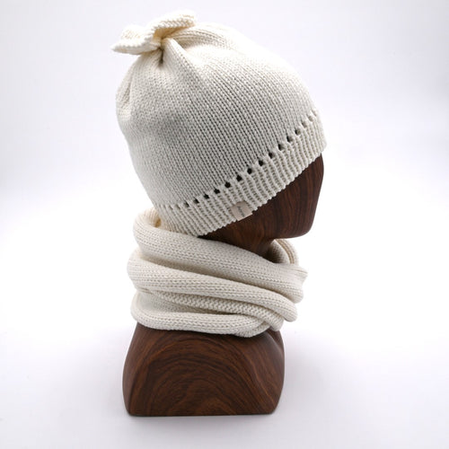 Profile of a mannequin wearing a French Vanilla - colored merino wool beanie with a distinctive 'petal gather' at the crown, paired with a matching Infinity Scarf.
