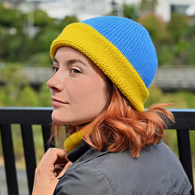 A Model wearing a Shaka knitted Toque with a blue crown and yellow brim, and matching Cowl.