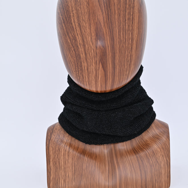 Black knit scarf on a wooden mannequin head against a white background