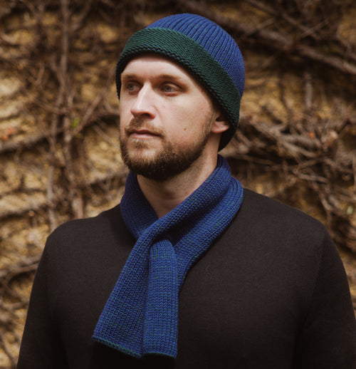 A model wearing an Azure Marbled Ascot Scarf and a matching Toque, standing in front of a wall with vines.