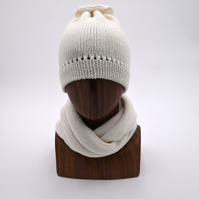 Mannequin wearing a French Vanilla -colored merino wool beanie with a distinctive 'petal gather' at the crown, paired with a matching Infinity Scarf.