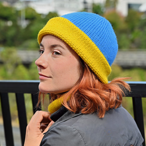 A Model wearing a Shaka knitted Toque with a blue crown and yellow brim, and matching Cowl.