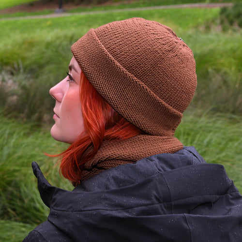 Person wearing a Nutmeg Ruapehu Beanie and matching scarf in a grassy outdoor setting