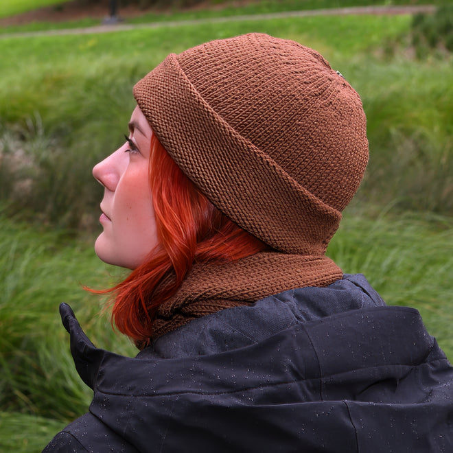 Person wearing a Nutmeg Ruapehu Beanie and matching scarf in a grassy outdoor setting