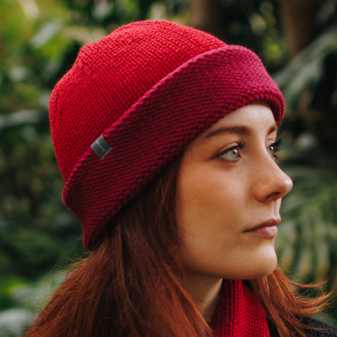 A model wearing a Mable Cuffed Toque in Mulberry with a silver bean, paired with a matching Ascot scarf.